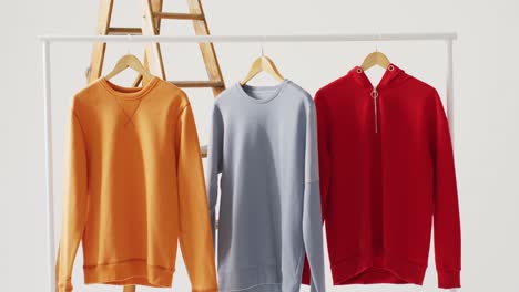 video of close up of yellow, blue and red sweaters hanging on white background