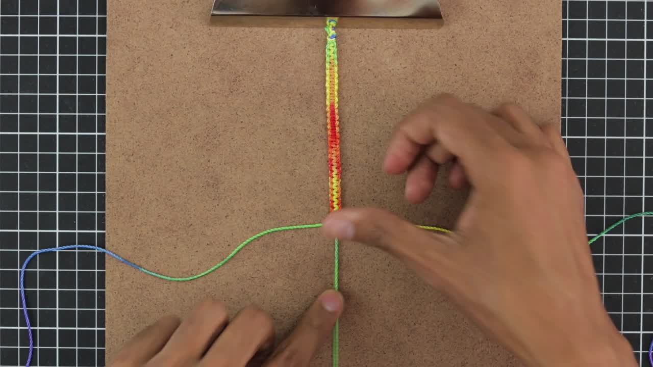manos tejiendo brazalete de macrame con patrones de arco iris, con hilos coloridos, timelapse