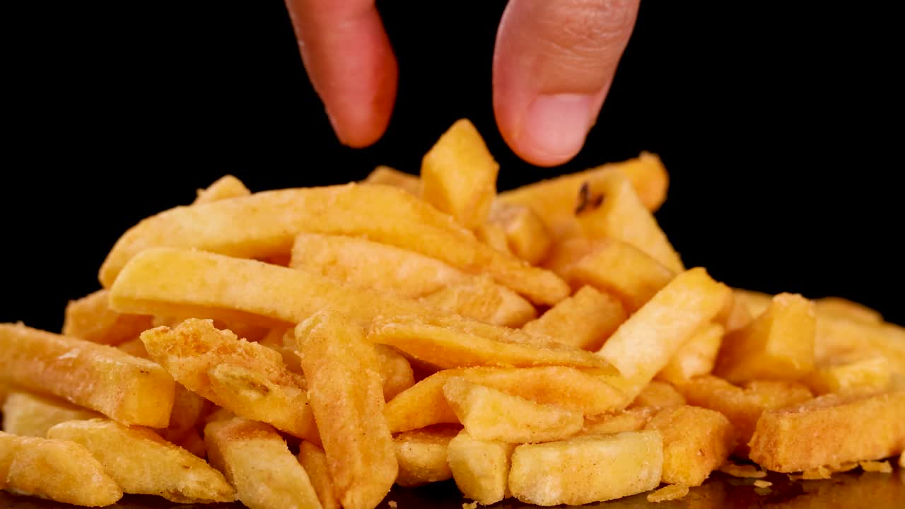 Close-up of hand selecting golden French fry from pile, dramatic lighting, static camera, dark backdrop