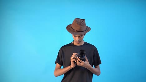 fun young indian boy in basic black t-shirt isolated on blue background studio and checking his dslr camera
