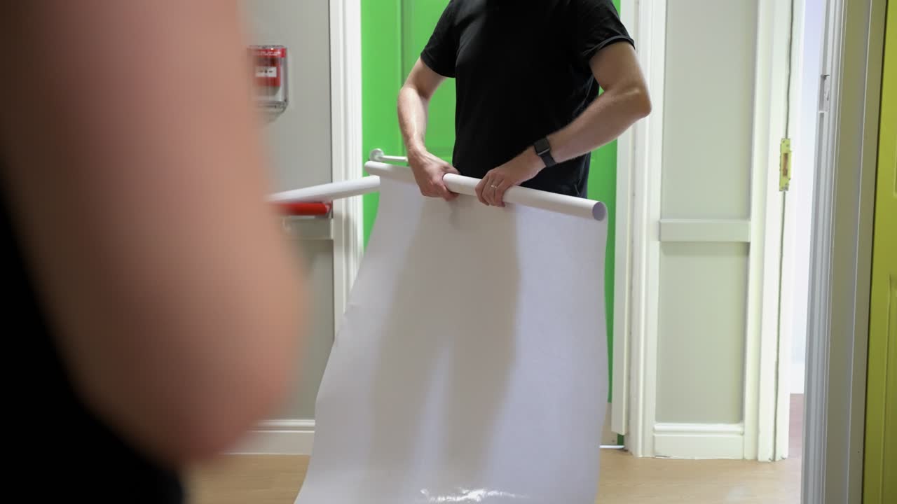 торговец скручивает лишний пластиковый виниловый материал, очищая рабочее пространство в офисе интерьером с цветными дверями и на переднем плане