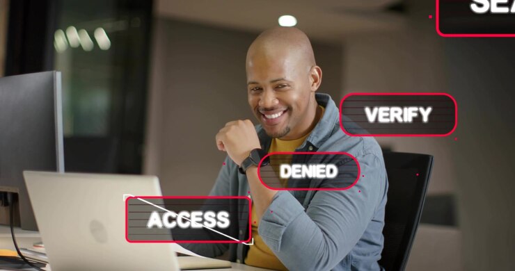 Man at desk verifying security access on laptop as ACCESS and DENIED badges appearing, smiling