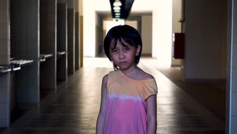 portrait of a young southeast asian boy alone scared looking into camera in an abandoned mall hallway with light and shadow in the background