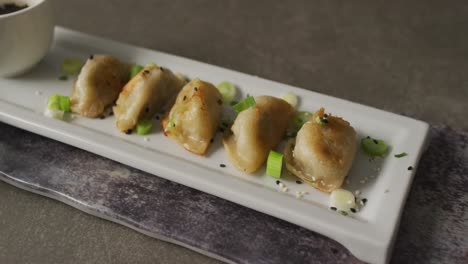 Composition-of-plate-with-gyoza-dumplings-and-soy-sauce-with-chopsticks-on-grey-background