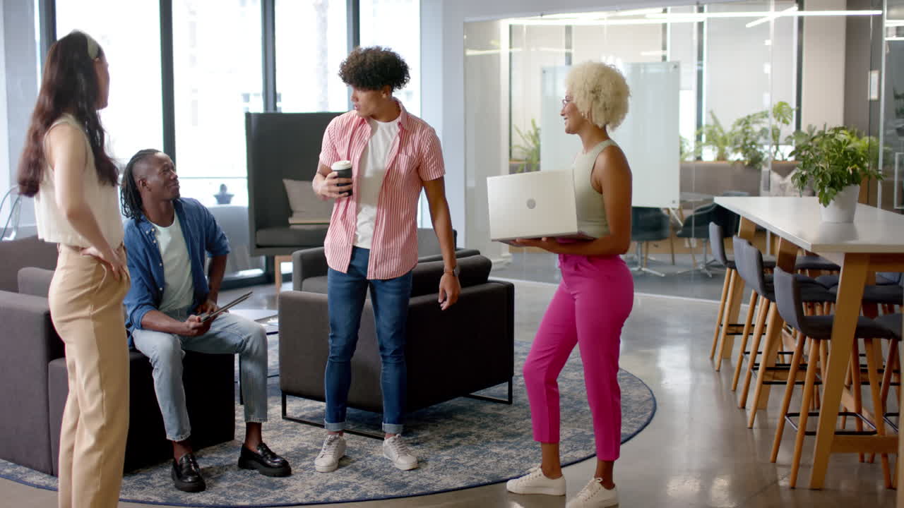 Group of colleagues in office, holding coffee and laptop, having casual conversation