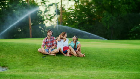 family with tablet sitting on grass. kids and parents spending time together