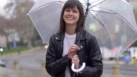 Porträt-Einer-Fröhlichen,-Lächelnden-Brünetten,-Die-Auf-Der-Straße-Einen-Durchsichtigen-Regenschirm-Dreht