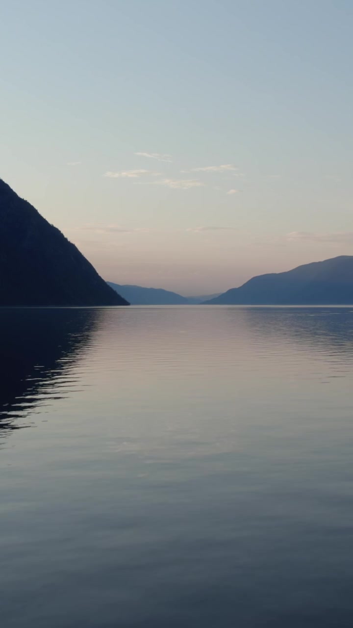 Serene wide shot of Teletskoye Lake with smooth water and distant mountain silhouettes at dusk, Altai Republic, Russia, soft pastel sky and tranquil nature mood