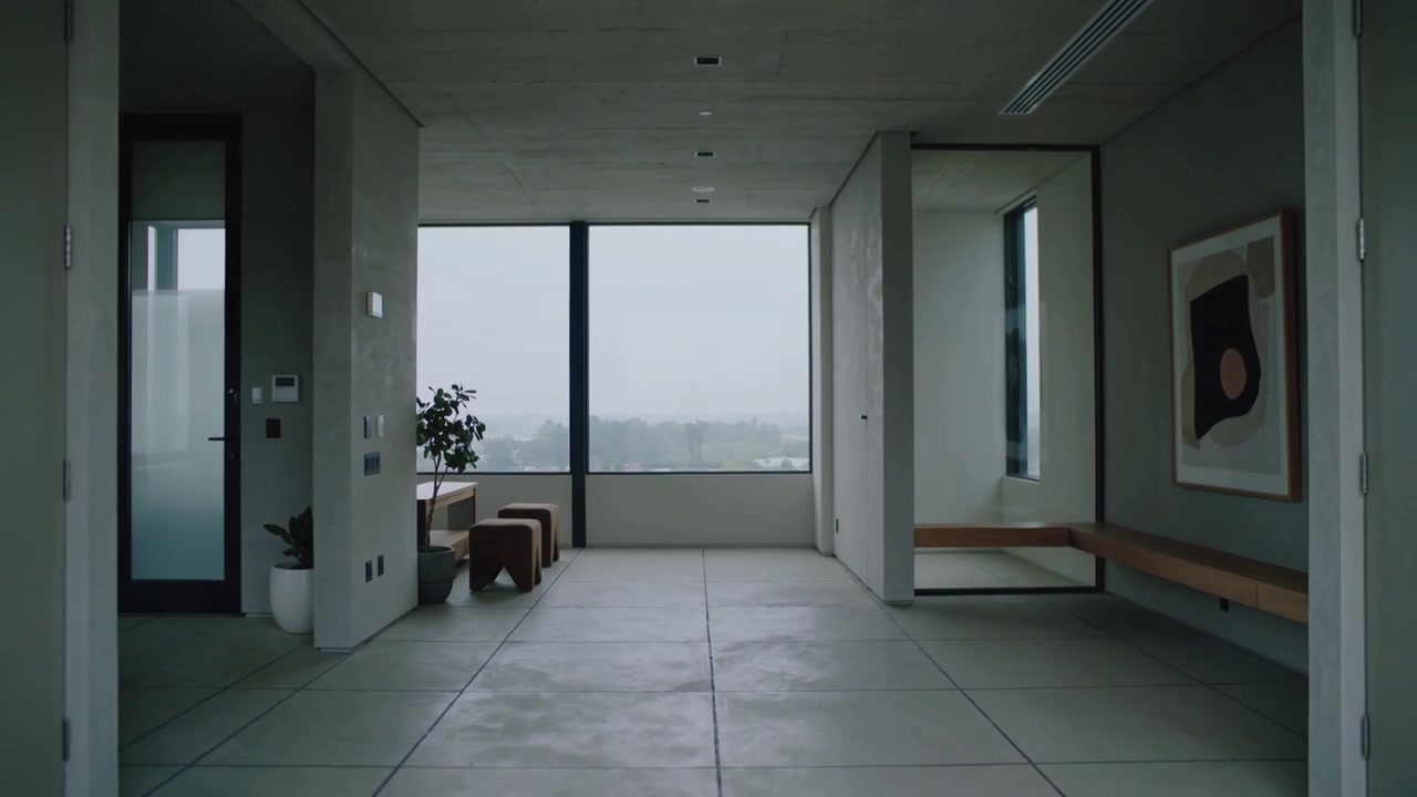 La cámara se aleja revelando el vestíbulo de un apartamento con una ventana de suelo a techo y un suelo de baldosas.