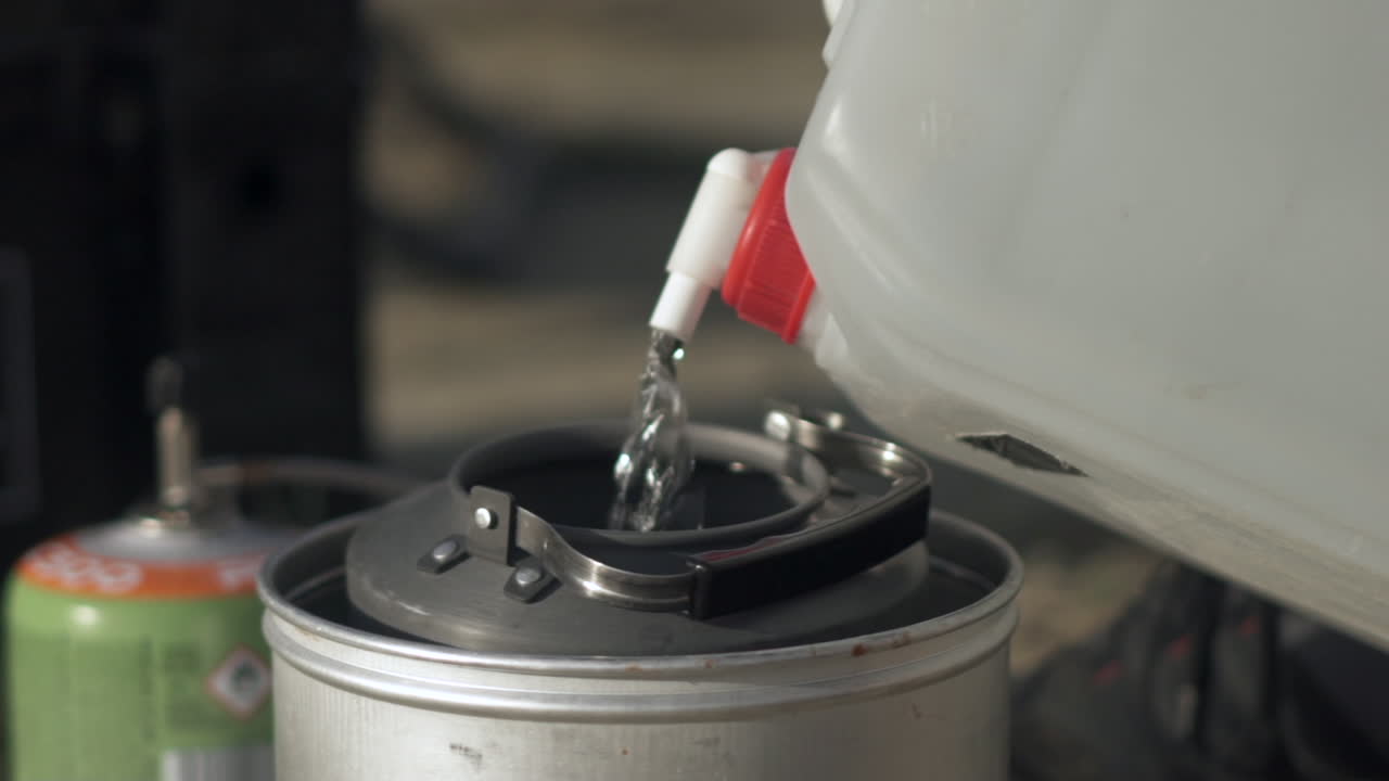 플라스틱 용기에서 금속 캠핑 용기에 물을 붓는 것