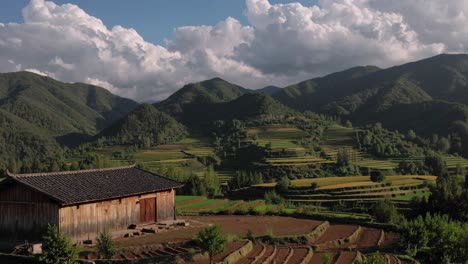 traditional wooden barn stands in front of a vast landscape of cultivated terraced fields extending towards the distant mountains under a cloudy sky