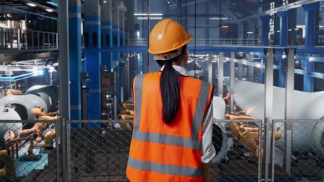 back view of asian female engineer with safety helmet talking on smartphone while standing in factory manufacture of wind turbines