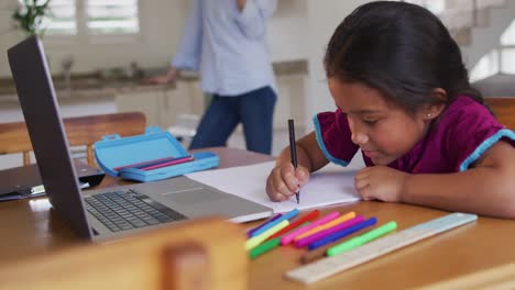 Niña-Hispana-Sentada-En-La-Mesa-Dibujando-Con-Su-Madre-En-Segundo-Plano.