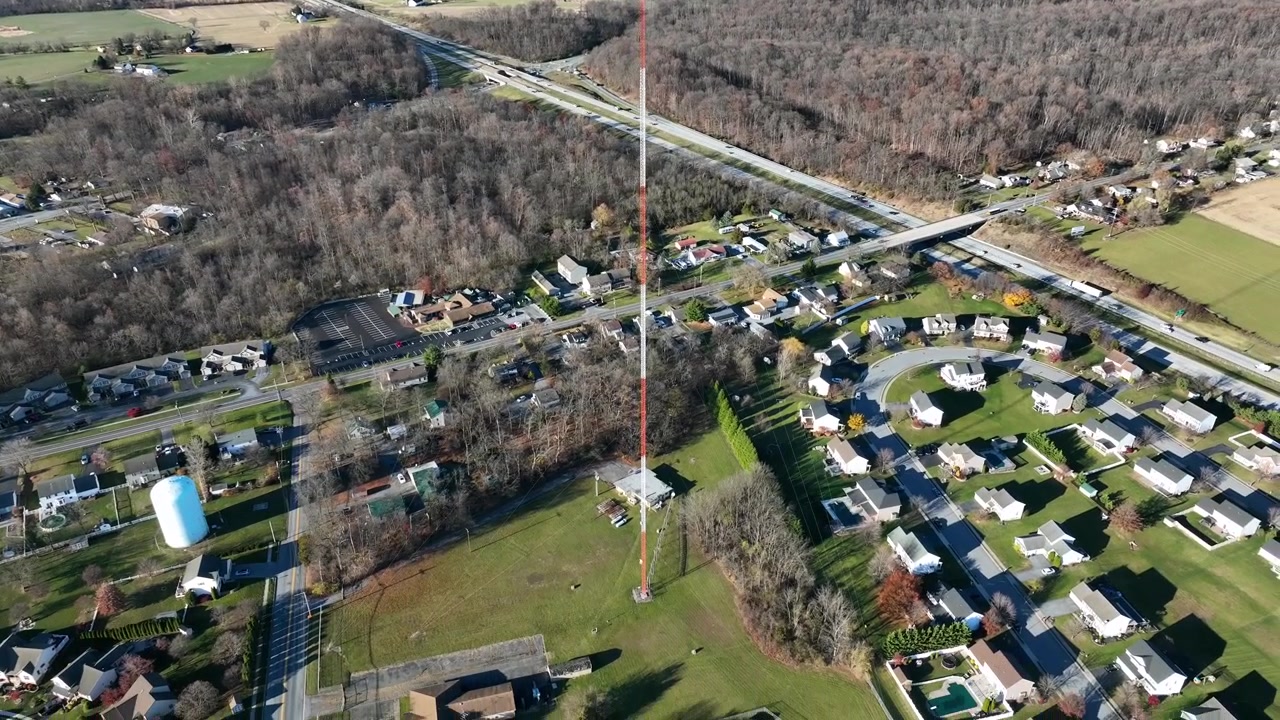 Ripresa aerea in picchiata di una torre di trasmissione circondata da un quartiere rurale negli USA. Alberi della foresta in una zona panoramica in autunno. Traffico sull'autostrada in periferia. Inquadratura ampia.