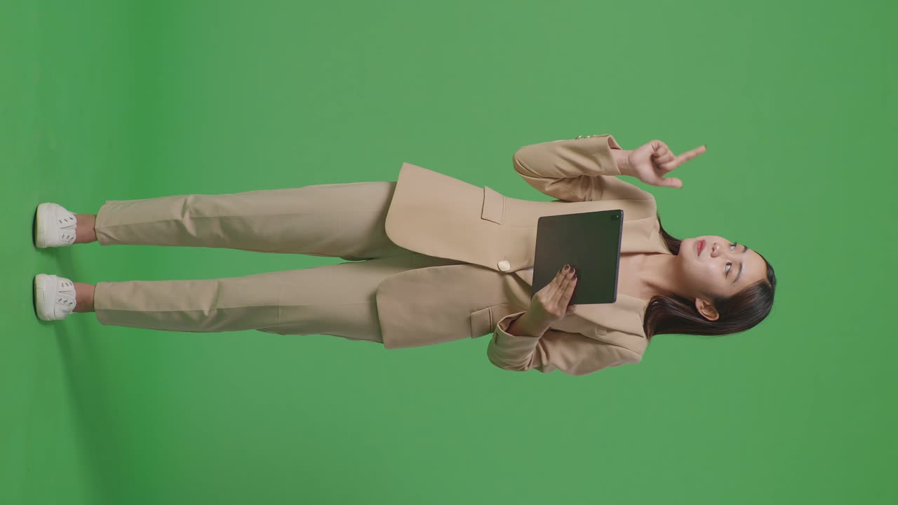 cuerpo lleno de mujer de negocios asiática usando tableta y apuntando al lado en el fondo de la pantalla verde en el estudio