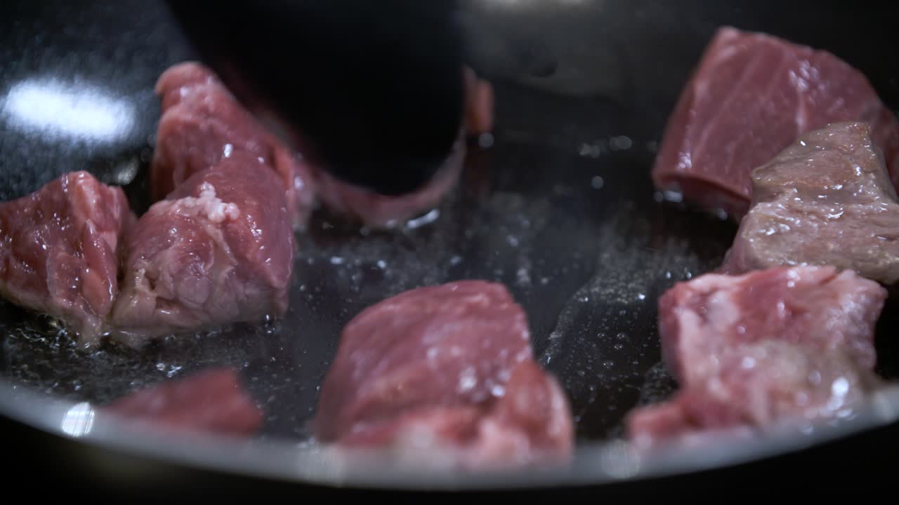 Menumis Daging Mentah Potongan Dadu Segar dalam Wajan Anti Lengket Hitam Panas dengan Minyak