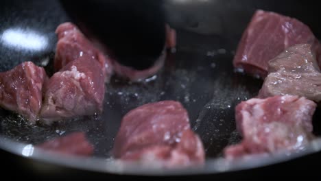 saltear cubos de carne cruda fresca en una sartén antiadherente negra caliente con aceite