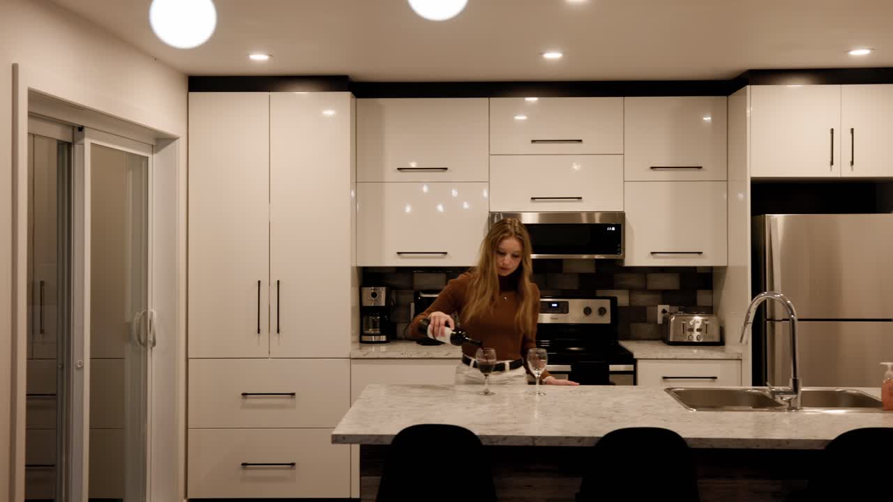 Donna caucasica che versa vino rosso in un bicchiere da vino in una moderna cucina di casa