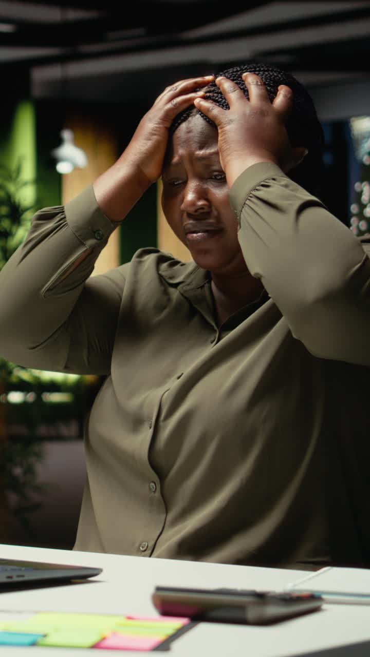 Vertical Video Black businesswoman distressed and burdened at the office after hours