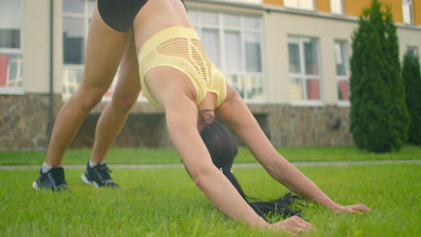 eine junge frau im park mit kopfhörern praktiziert yoga. sie praktiziert yoga auf dem gras vor dem hintergrund von häusern im stadtpark in zeitlupe