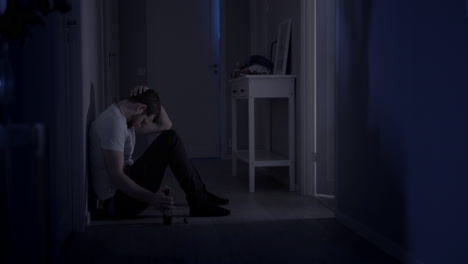 regret failure and mistake, wide portrait shot of troubled man on floor leaning against wall in dark room