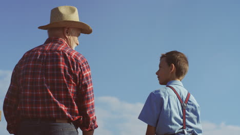 rear view on a grandfather and grandson standing on the shore of a lake and fishing throwing rods to the water