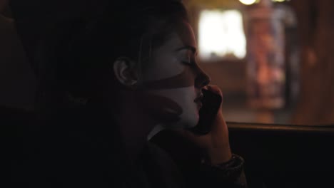 close up view of young woman talking on the phone while riding in taxi late at night. night city lights on the background