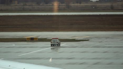 a car drives on the airport apron while another one is parked nearby with lights flashing on top