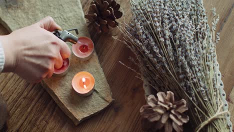 Top-shot-Movement-of-Lavender,-Pine-Cones-and-Lighting-Tealight-Candles-with-Torch