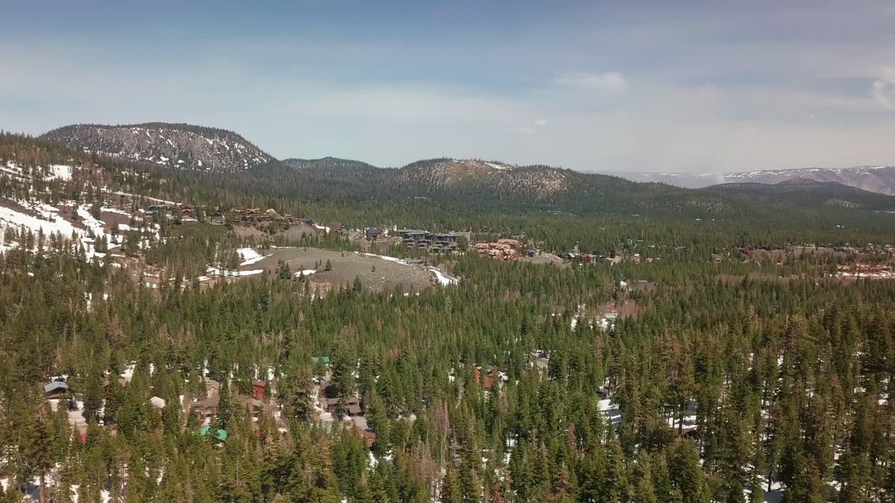 toma aérea de un pueblo montañoso de gran altitud ubicado al pie de picos nevados y un bosque de invierno