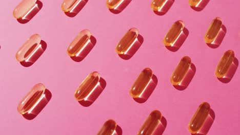 vídeo de cápsulas de aceite dispuestas en filas sobre un fondo rosado.