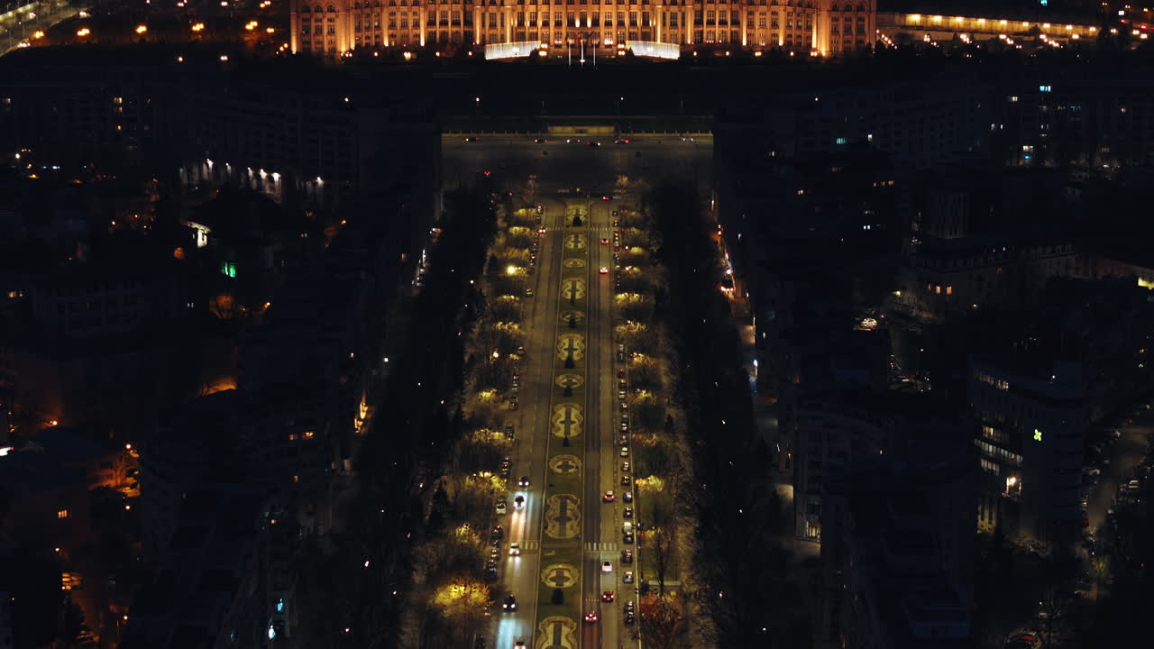 Aerial drone view of illuminated Palace of the Parliament in Bucharest downtown in the evening. Moving traffic on the road. Romania