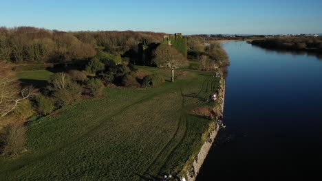 People-enjoying-the-sun-by-Corrib-River,-aerial-reverse-dolly-in-Galway,-Ireland