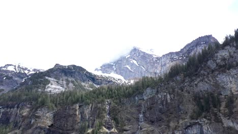 Drone-flight-over-a-beautiful-alpine-valley,-waterfalls-and-high-snow-capped-mountains