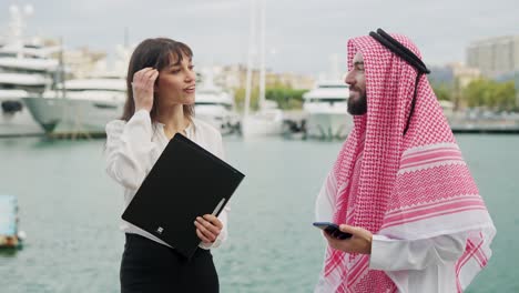 arab businessman discussing terms and conditions for yacht charter with female broker in port