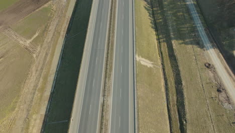 aerial view of a highway with vehicles in motion, the road cuts through agricultural fields with distinct tire tracks visible on the sides of the pavement