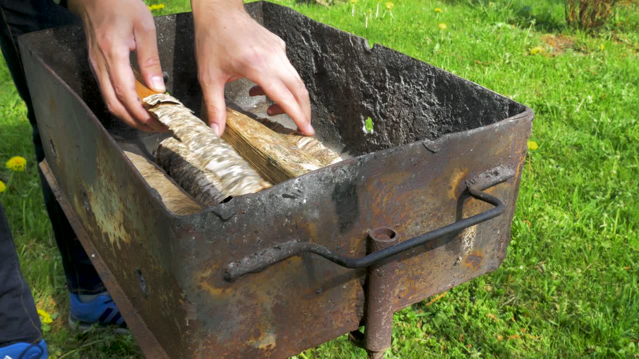 젊은 남자가 나무 통나무를 내려놓고 베이킹과 바비큐를 위해 녹슨 그릴을 준비하고, 중간 클로즈업 샷