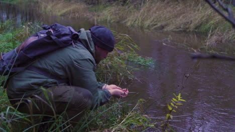 Hiker-drinking-water-from-the-river-in-the-woodland-forest-to-hydrate,-close-up-of-man-in-natural-environment