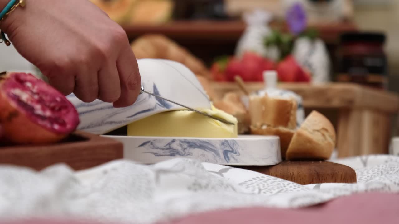 Hands spread some butter placed on a picnic blanket surrounded with a lot of picnic food.