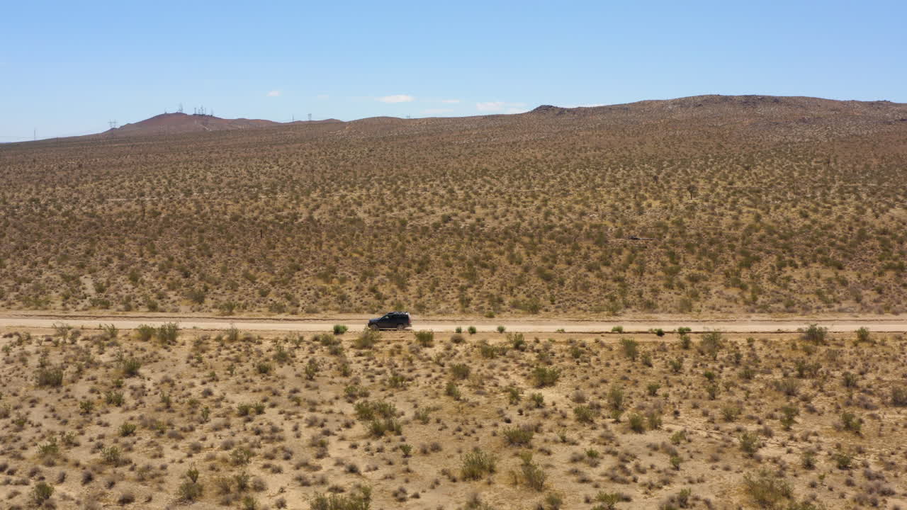 el todoterreno negro acelera rápidamente por una carretera perfectamente recta a través de las llanuras del desierto de mojave en un día azul claro