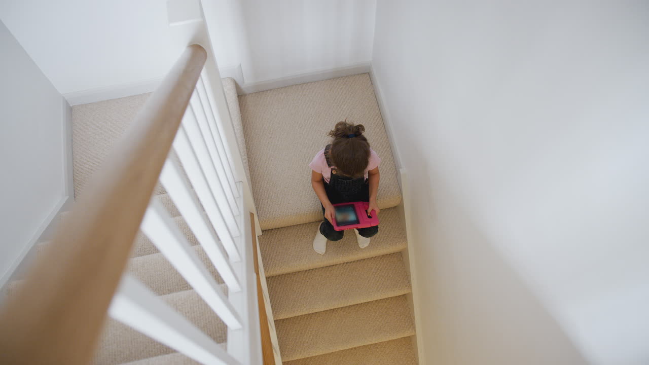niña sentada en las escaleras de su casa jugando con una tableta digital