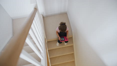 Niña-Sentada-En-Las-Escaleras-En-Casa-Jugando-Con-Tableta-Digital