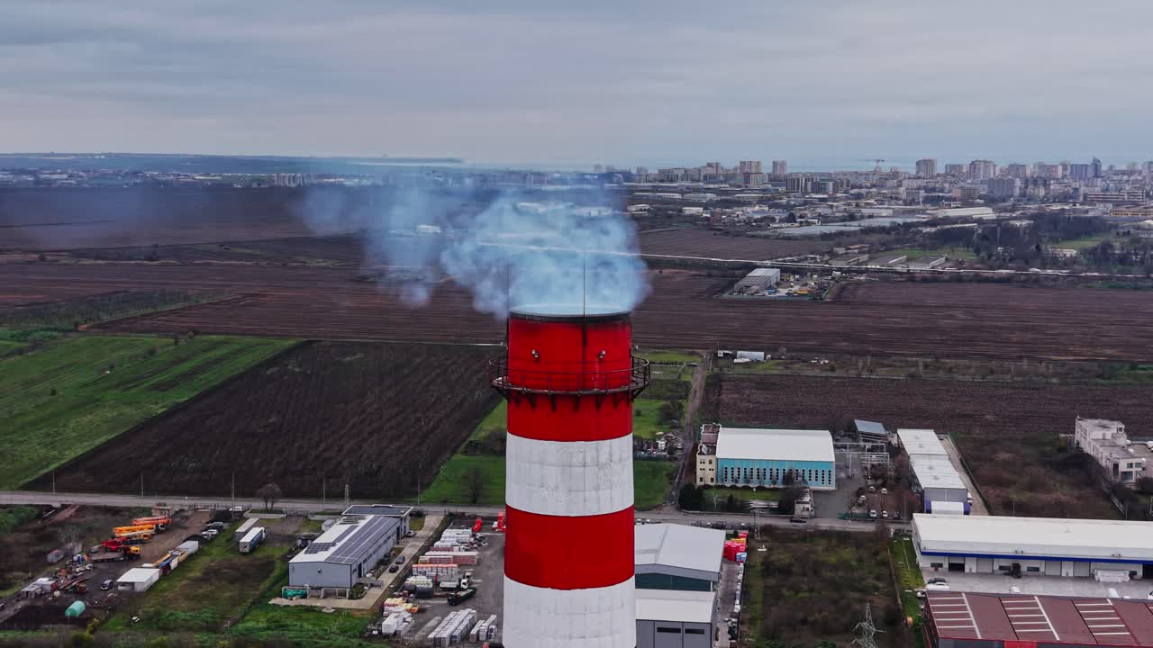 Ciminiera industriale che rilascia fumo su un paesaggio urbano in primavera