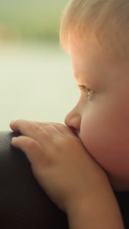tired little boy leans on chair back looking out of motorboat window closeup. sad toddler kid sits in cabin travelling by tourist boat on vacation
