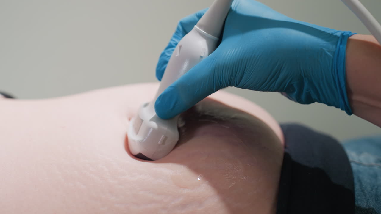 close up of medical technologist wearing lab gloves scanning patient abdomen with ultrasound detector on lubricated skin surface focusing on lower tummy region for diagnostic imaging assessment