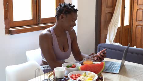 Mujer-Negra-Contenta-Usando-Un-Teléfono-Inteligente-En-La-Mesa-Con-Frutas-Frescas