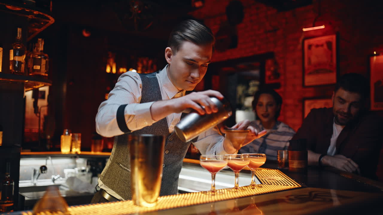Primo piano di un barman professionista che versa un drink dallo shaker ai bicchieri al bancone del bar