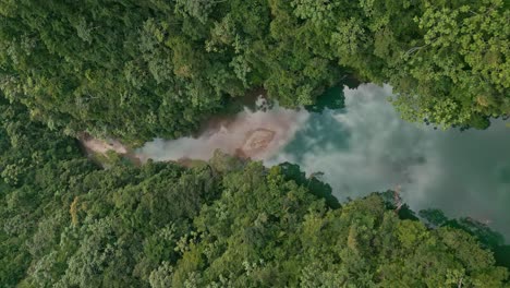 vertical shot over river in bonao with water reflection surrounded by deep lush jungle in dominican republic