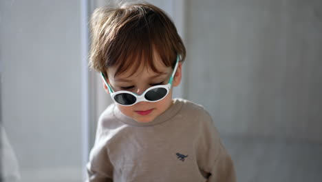 lovely little kid in grey sweater and sunglasses. close op portrait on the child indoors.
