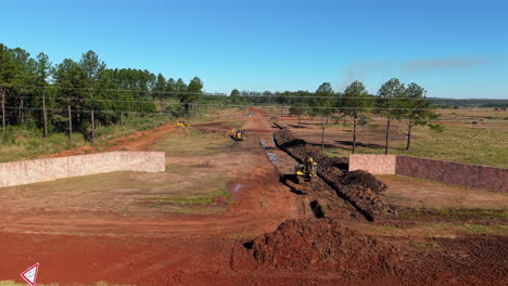 excavators digging wide trench in red soil field under clear blue sky, argentina